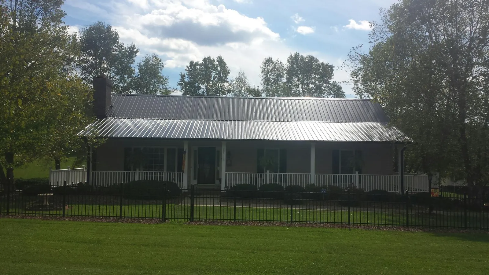 Gray metal roof on a brick ranch with a full width front porch — Gutter Guard Installation work by our crew in Waterville